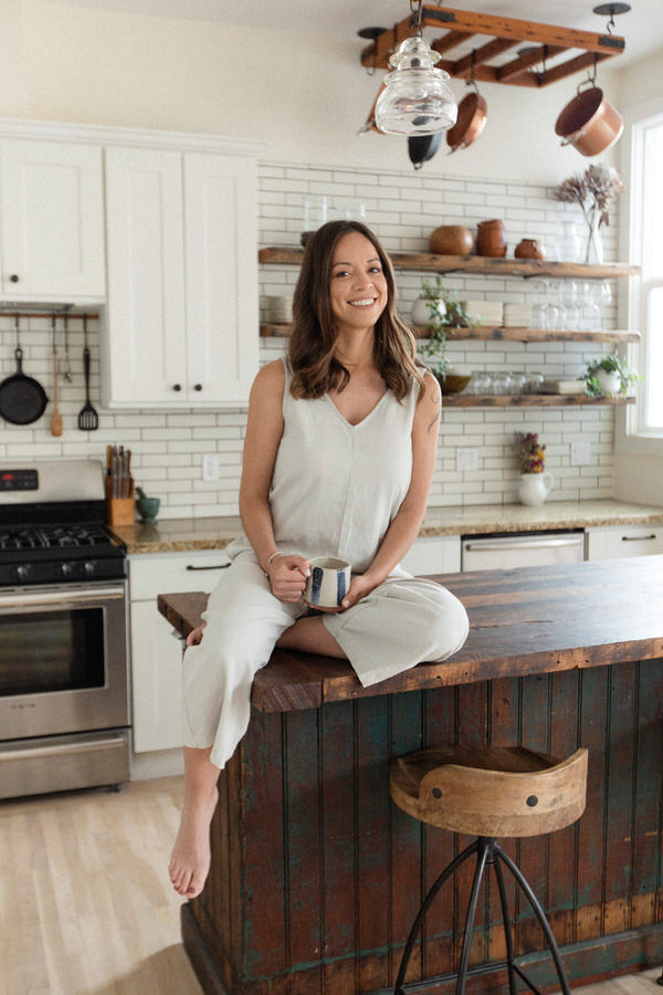Woman sitting on a counter top holding a cup and smiling.